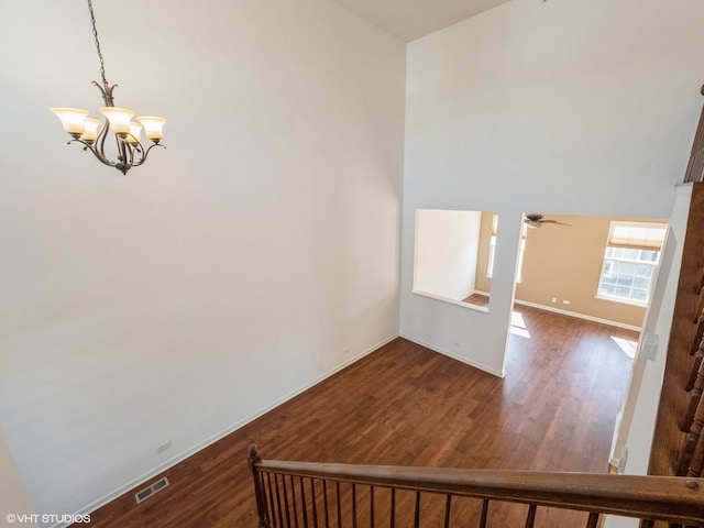 staircase featuring visible vents, ceiling fan with notable chandelier, baseboards, and wood finished floors