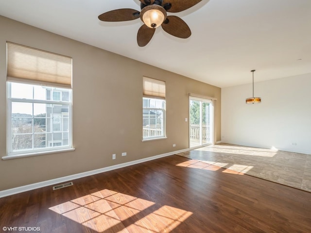 spare room with a ceiling fan, wood finished floors, visible vents, and baseboards