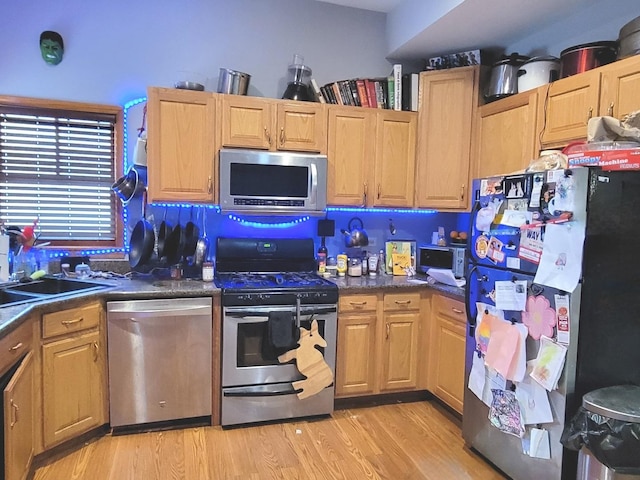 kitchen with dark countertops, appliances with stainless steel finishes, light wood-style floors, and a sink