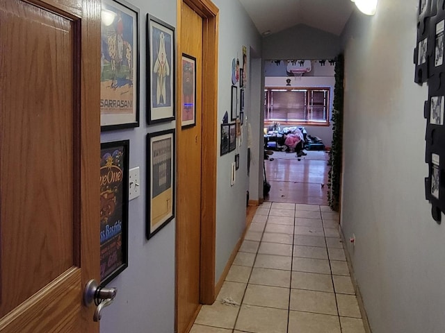 hall featuring light tile patterned floors, baseboards, and vaulted ceiling