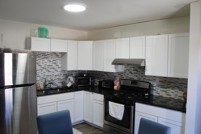 kitchen with dark countertops, stainless steel appliances, under cabinet range hood, white cabinetry, and a sink