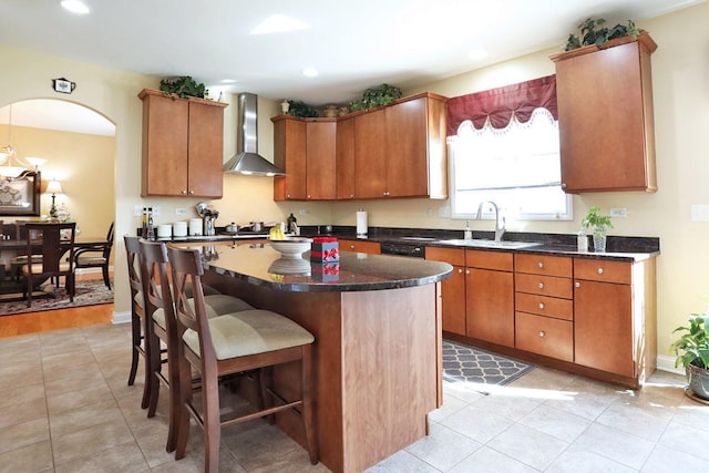 kitchen featuring wall chimney exhaust hood, a breakfast bar, a center island, a sink, and recessed lighting