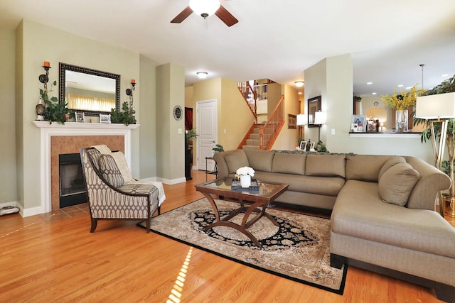 living area featuring ceiling fan, a fireplace, wood finished floors, baseboards, and stairway