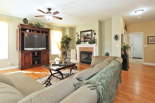 living area featuring a ceiling fan, baseboards, a tiled fireplace, and wood finished floors