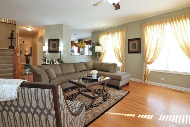 living area featuring light wood-type flooring, stairway, plenty of natural light, and a ceiling fan