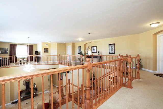 hall with a notable chandelier, baseboards, carpet flooring, and an upstairs landing