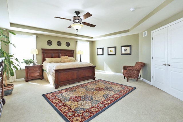 bedroom featuring visible vents, baseboards, a raised ceiling, and light colored carpet