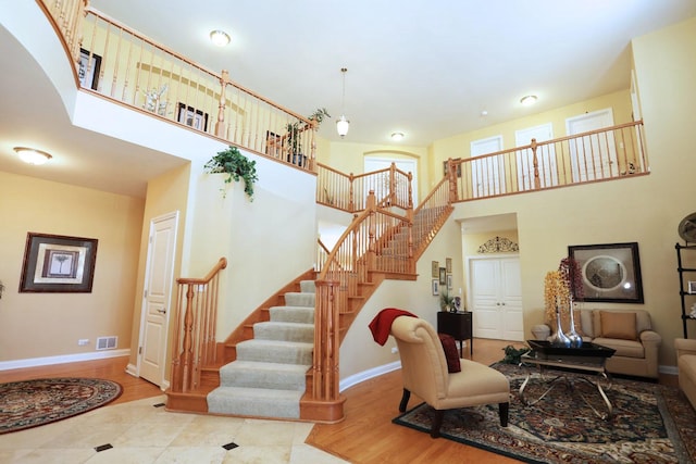 living area featuring visible vents, a high ceiling, wood finished floors, baseboards, and stairs