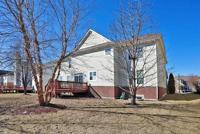 rear view of house with brick siding, a lawn, and a wooden deck