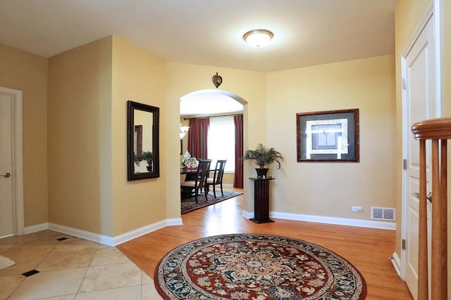 foyer entrance with light wood-type flooring, arched walkways, visible vents, and baseboards