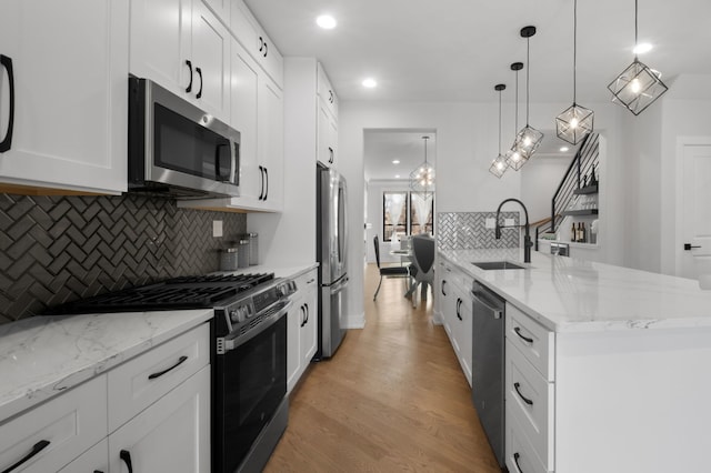 kitchen featuring light stone counters, a sink, white cabinets, light wood-style floors, and appliances with stainless steel finishes