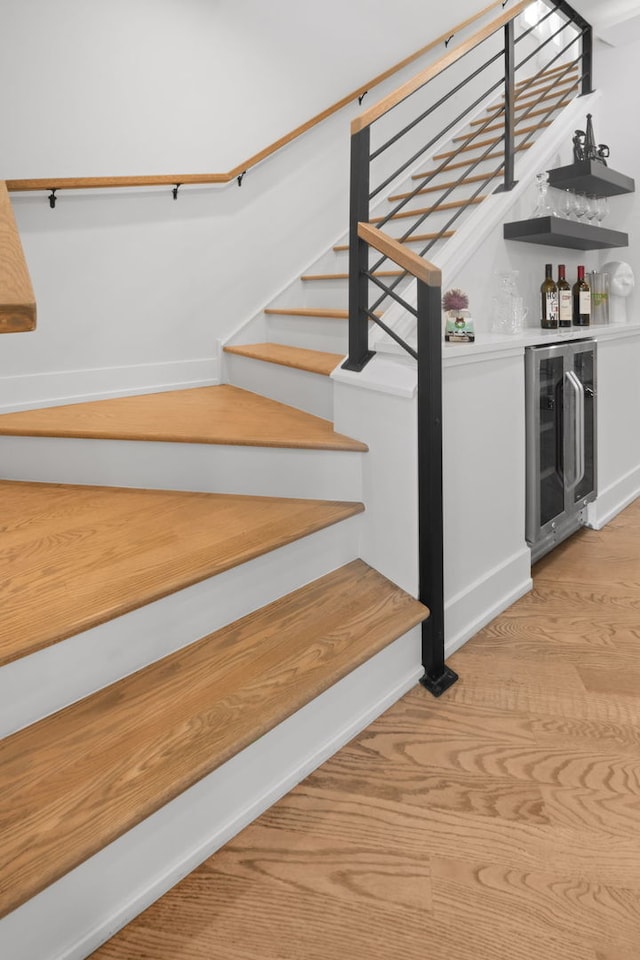 stairway with wine cooler, baseboards, a dry bar, and wood finished floors