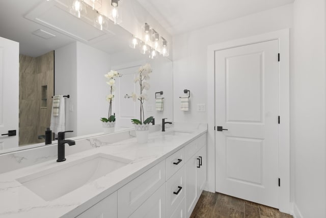 full bath with wood finished floors, tiled shower, a sink, and double vanity