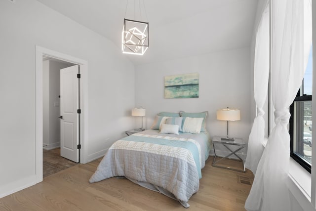 bedroom featuring lofted ceiling, a notable chandelier, wood finished floors, visible vents, and baseboards