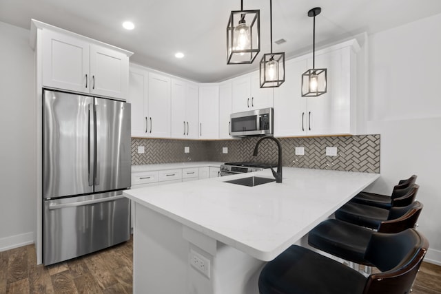 kitchen featuring stainless steel appliances, dark wood-type flooring, a peninsula, white cabinets, and tasteful backsplash