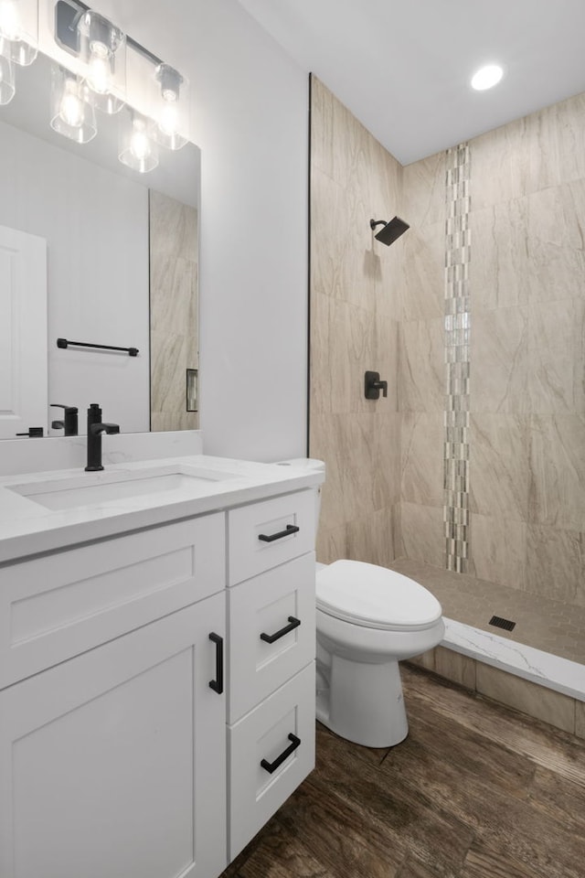 bathroom with a tile shower, vanity, wood finished floors, and toilet