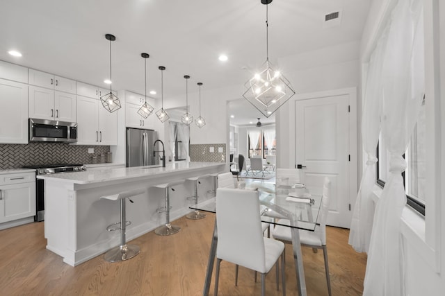 kitchen with visible vents, decorative backsplash, appliances with stainless steel finishes, white cabinetry, and light wood-type flooring