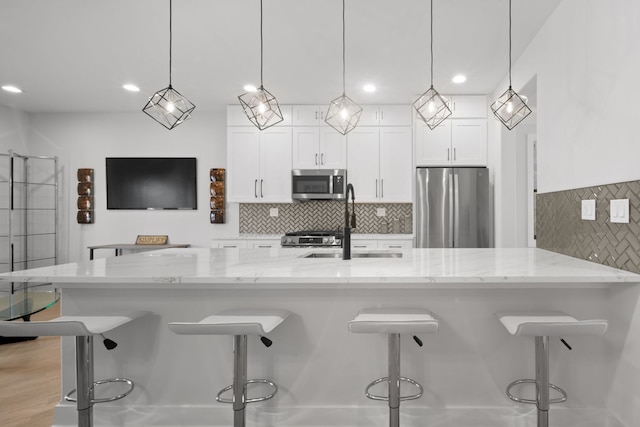 kitchen with white cabinets, light stone counters, stainless steel appliances, and a sink