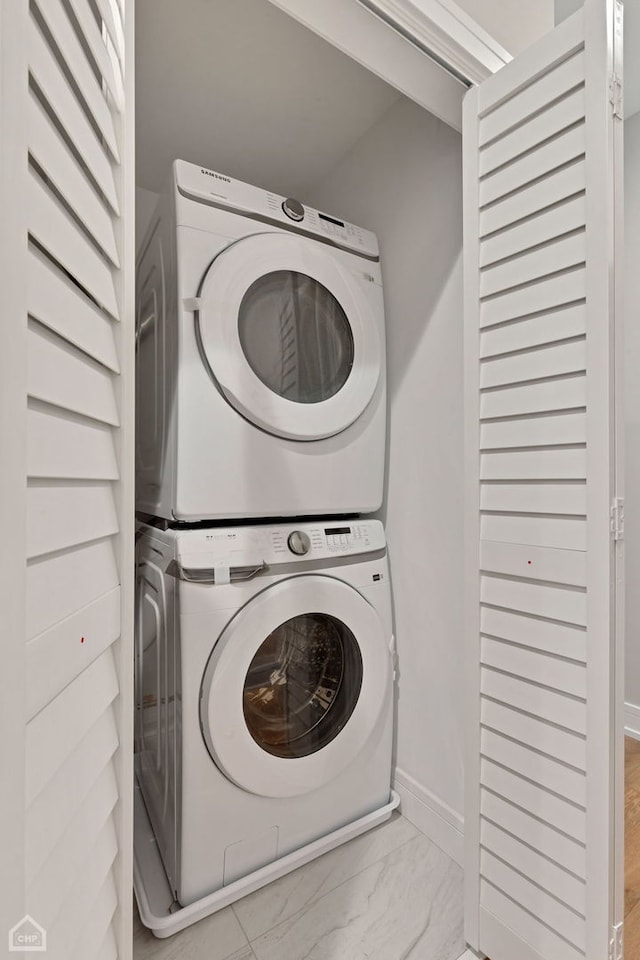 laundry area with marble finish floor, laundry area, baseboards, and stacked washer / drying machine