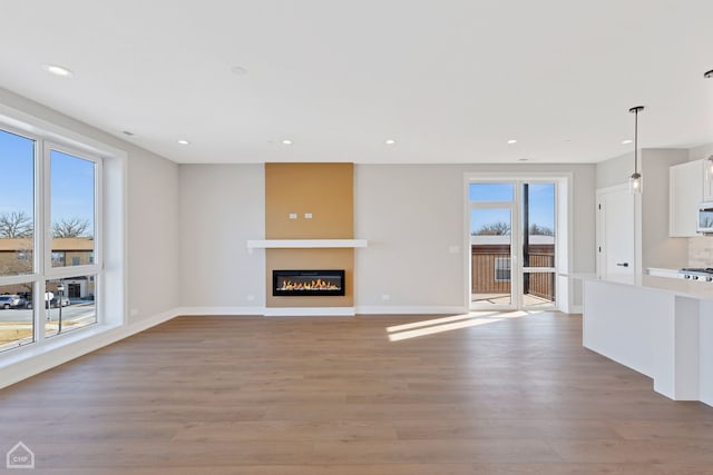 unfurnished living room featuring recessed lighting, baseboards, a glass covered fireplace, and light wood finished floors