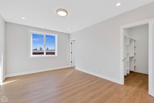 unfurnished bedroom with a spacious closet, light wood-type flooring, and baseboards