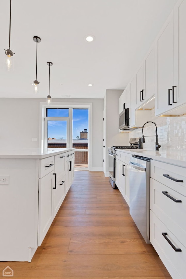 kitchen with light wood finished floors, light countertops, backsplash, appliances with stainless steel finishes, and white cabinets