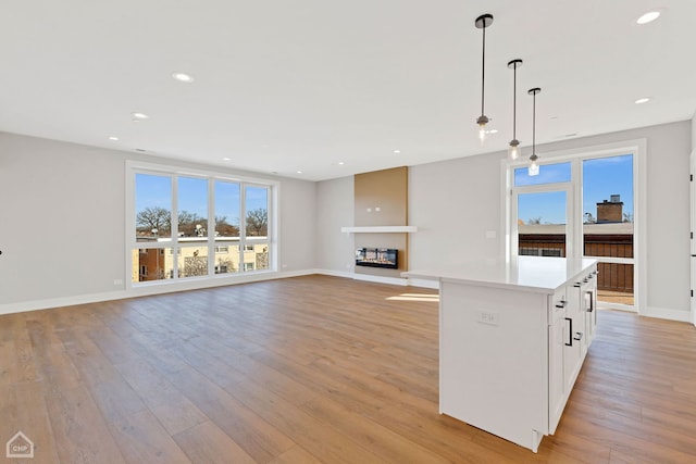 unfurnished living room with light wood-type flooring, a glass covered fireplace, a wealth of natural light, and recessed lighting