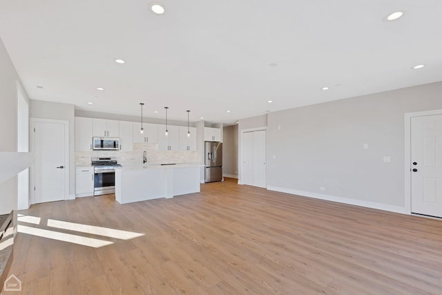 kitchen with white cabinetry, open floor plan, light countertops, appliances with stainless steel finishes, and decorative backsplash