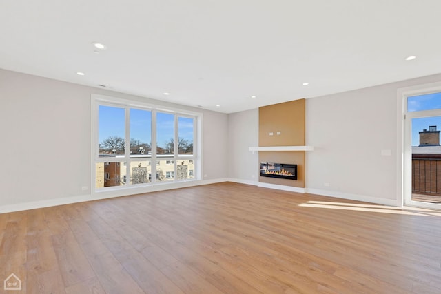 unfurnished living room with a glass covered fireplace, a wealth of natural light, and light wood-style floors