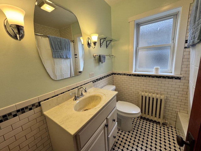 bathroom featuring toilet, a wainscoted wall, vanity, tile walls, and radiator heating unit