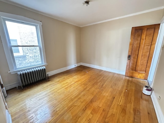 empty room featuring light wood-type flooring, radiator heating unit, baseboards, and crown molding