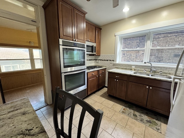 kitchen featuring a ceiling fan, a sink, light stone countertops, stainless steel appliances, and backsplash