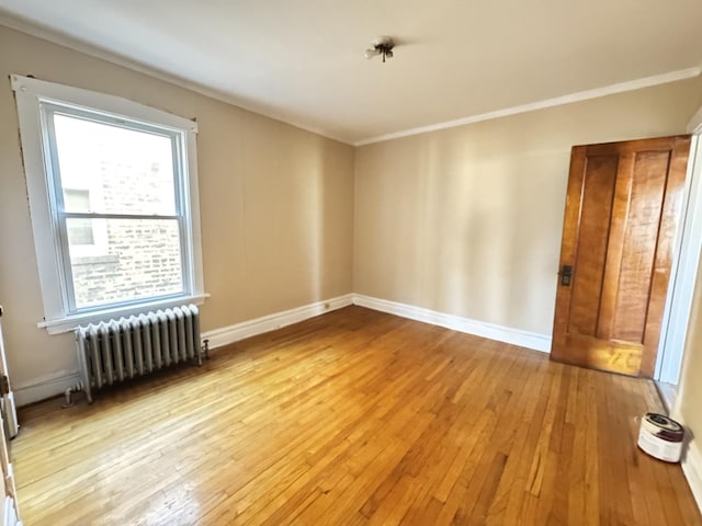 empty room with radiator, baseboards, crown molding, and light wood finished floors