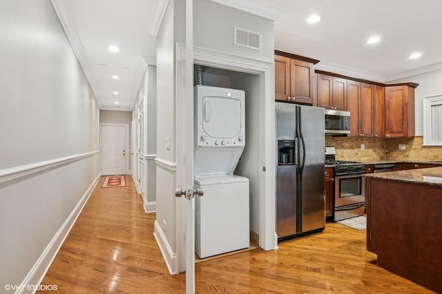 kitchen with stainless steel appliances, visible vents, stacked washing maching and dryer, decorative backsplash, and dark stone countertops