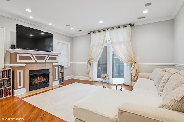 living area featuring ornamental molding, a tile fireplace, visible vents, and wood finished floors