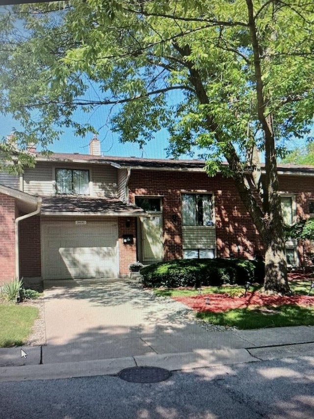 view of front facade with driveway, brick siding, a chimney, and an attached garage