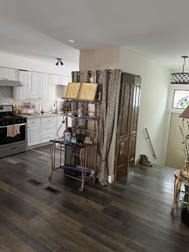 kitchen featuring stainless steel range with gas cooktop, dark wood finished floors, tasteful backsplash, light countertops, and white cabinetry