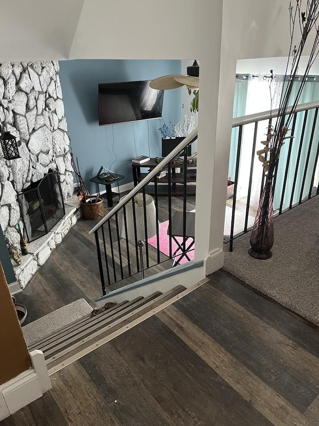 stairway with a stone fireplace and wood finished floors