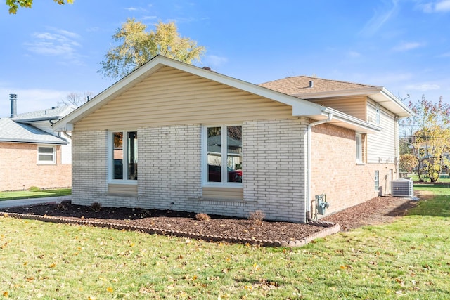 view of side of property featuring brick siding, a yard, and central AC