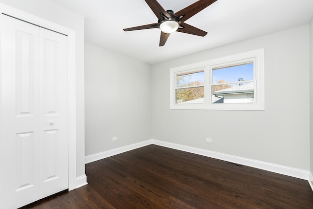 unfurnished bedroom with dark wood-type flooring, a ceiling fan, visible vents, baseboards, and a closet