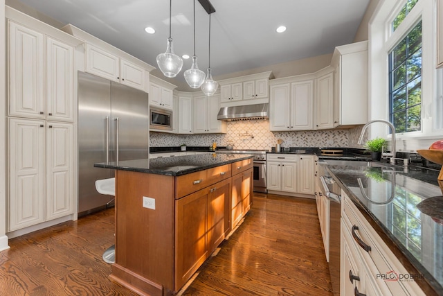 kitchen with a center island, dark wood finished floors, decorative backsplash, built in appliances, and extractor fan