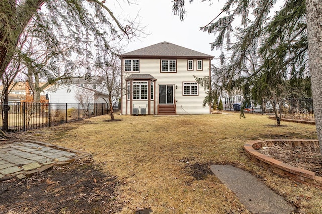 back of property with entry steps, a fenced backyard, and a yard