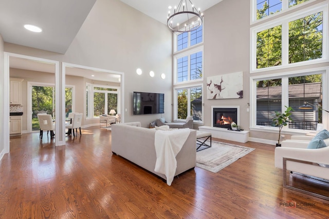 living area with a notable chandelier, baseboards, wood finished floors, and a glass covered fireplace