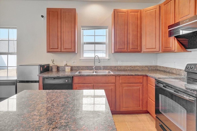 kitchen with black appliances, dark stone countertops, range hood, and a sink