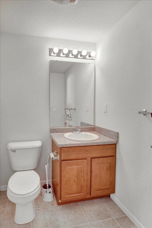 half bath with tile patterned flooring, toilet, vanity, and baseboards