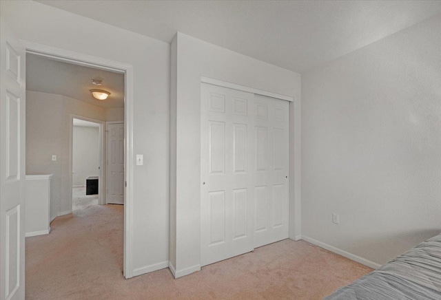 bedroom featuring light colored carpet, baseboards, and a closet