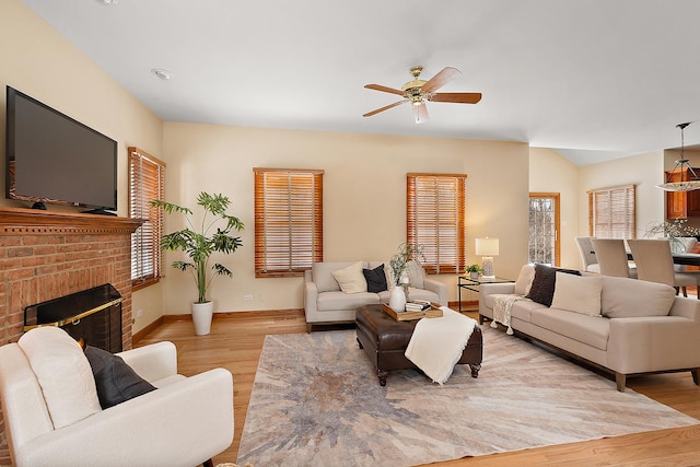 living area featuring light wood finished floors, a fireplace, baseboards, and a ceiling fan