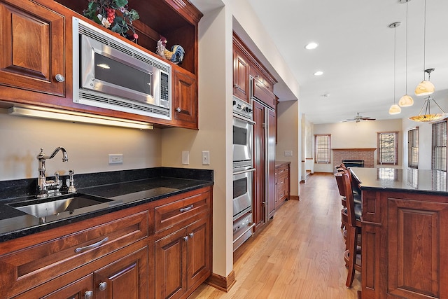 kitchen featuring stainless steel appliances, a brick fireplace, open floor plan, a sink, and dark stone counters