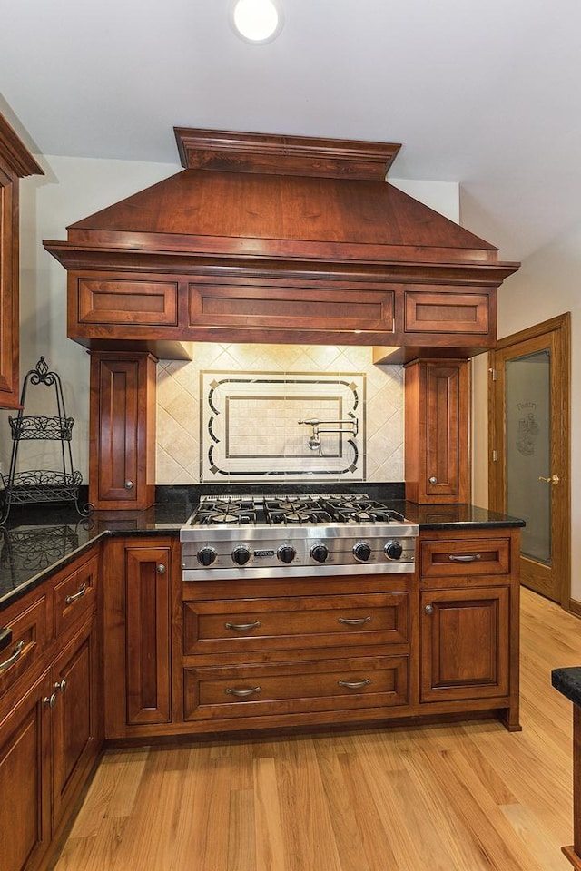 kitchen featuring light wood-style flooring, stainless steel gas cooktop, decorative backsplash, and dark stone counters