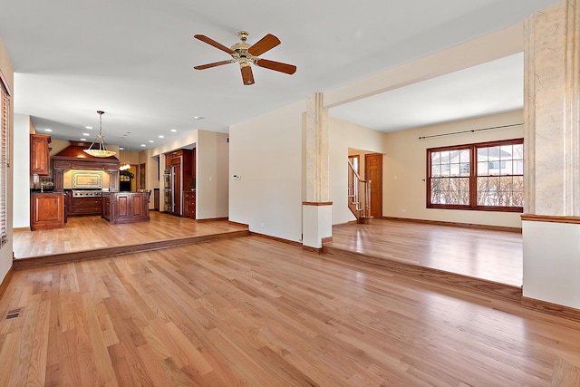 unfurnished living room with light wood-type flooring, baseboards, stairway, and a ceiling fan